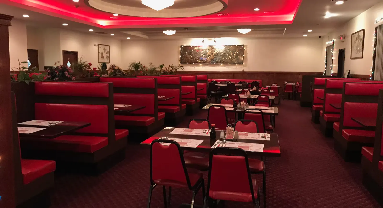 Bali Village dining room with red booths under a red-lit ceiling and a bronze mural