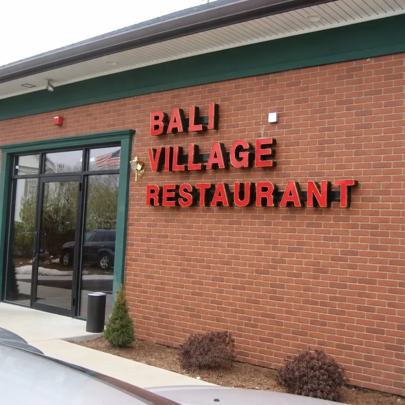 Bali Village Restaurant's brick storefront with green trim, a glass entrance door and shrubs along the front