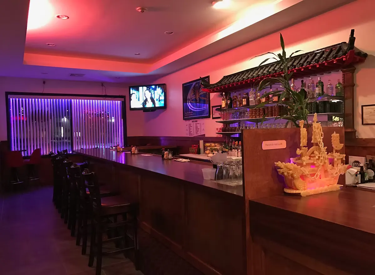 Dark wood bar with a carved jade ship and purple and red lighting